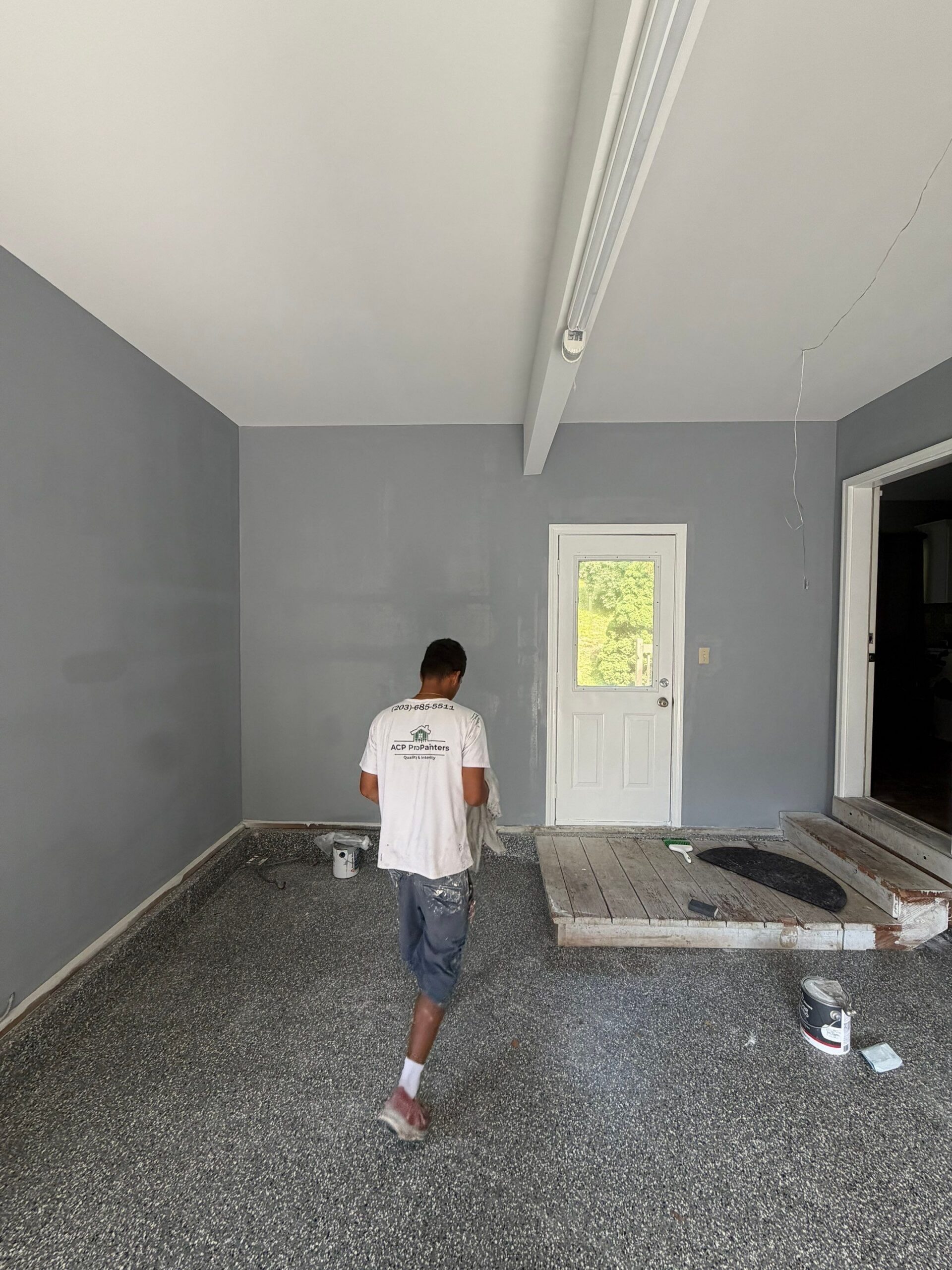 Painter walking through a room with gray painted walls and epoxy flooring