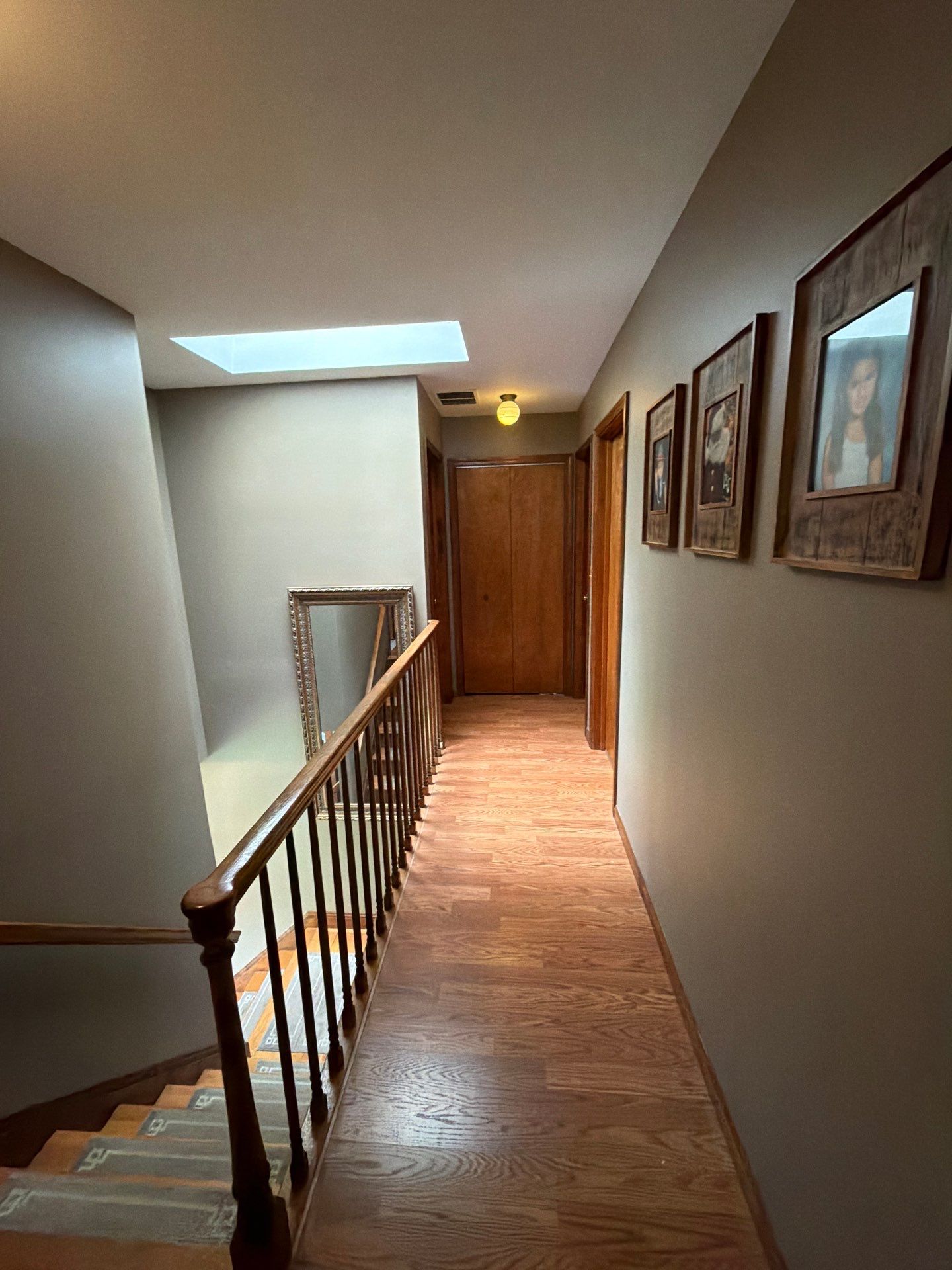 Upstairs hallway with hardwood flooring, railing, and picture frames