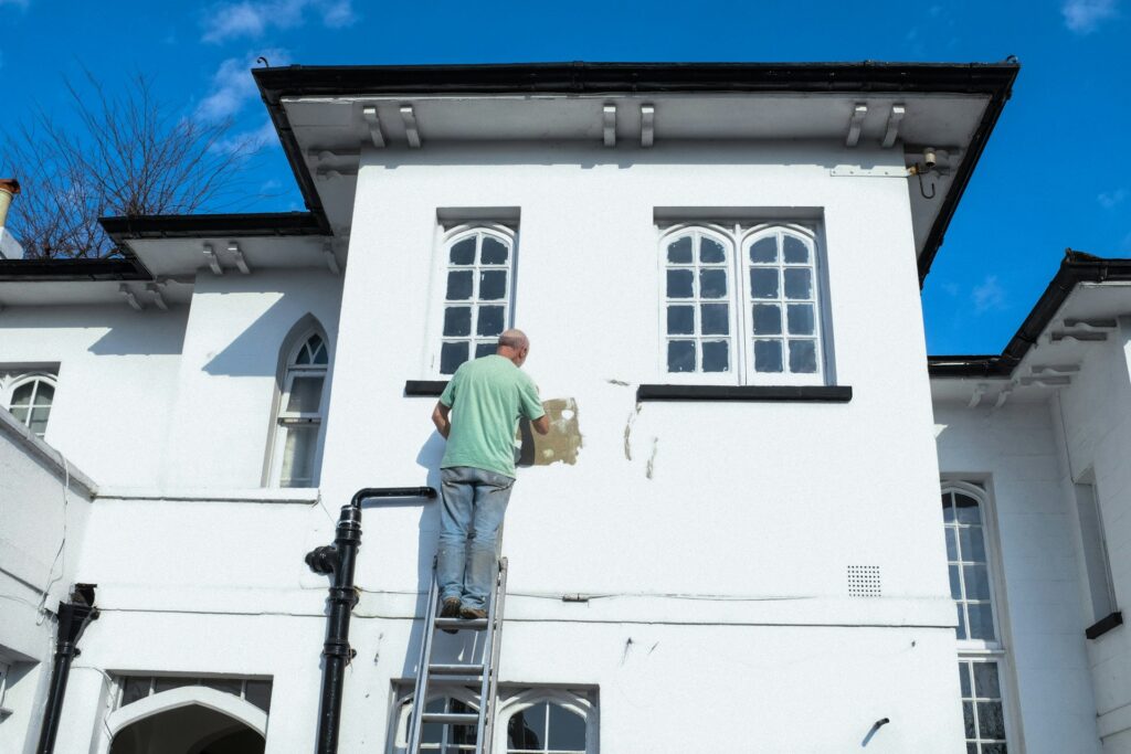 Painter on a ladder repairing exterior wall of a white house